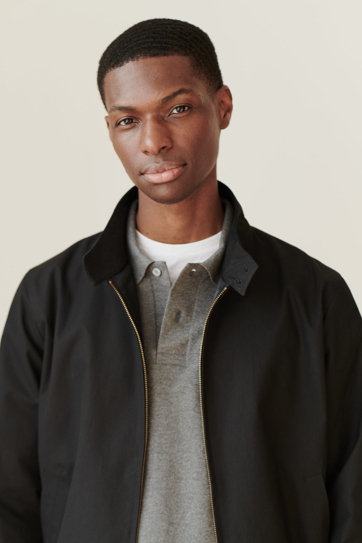 
            Portrait of black male wearing black Harrington jacket over grey long sleeve polo shirt