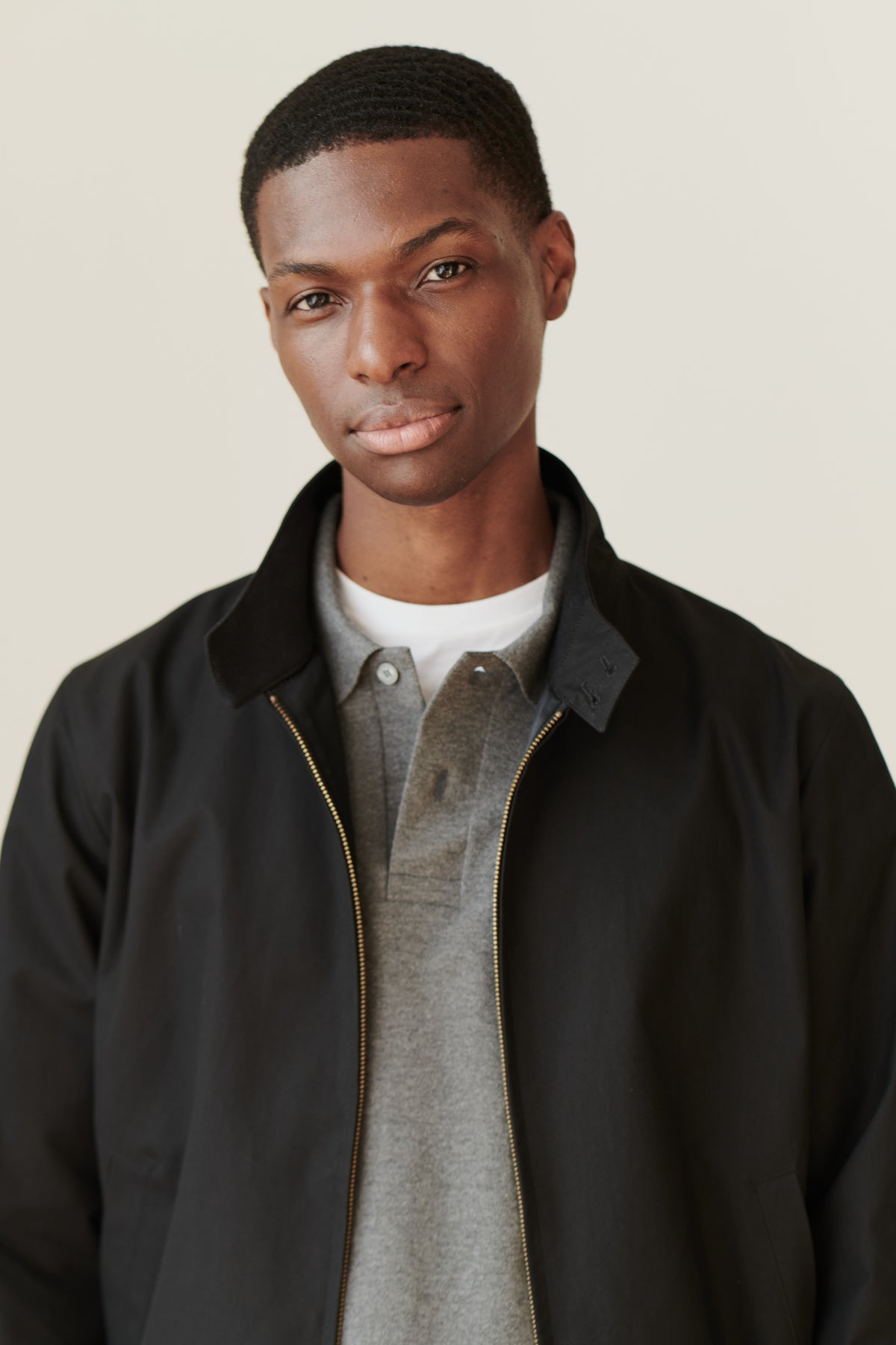 Portrait of black male wearing black Harrington jacket over grey long sleeve polo shirt