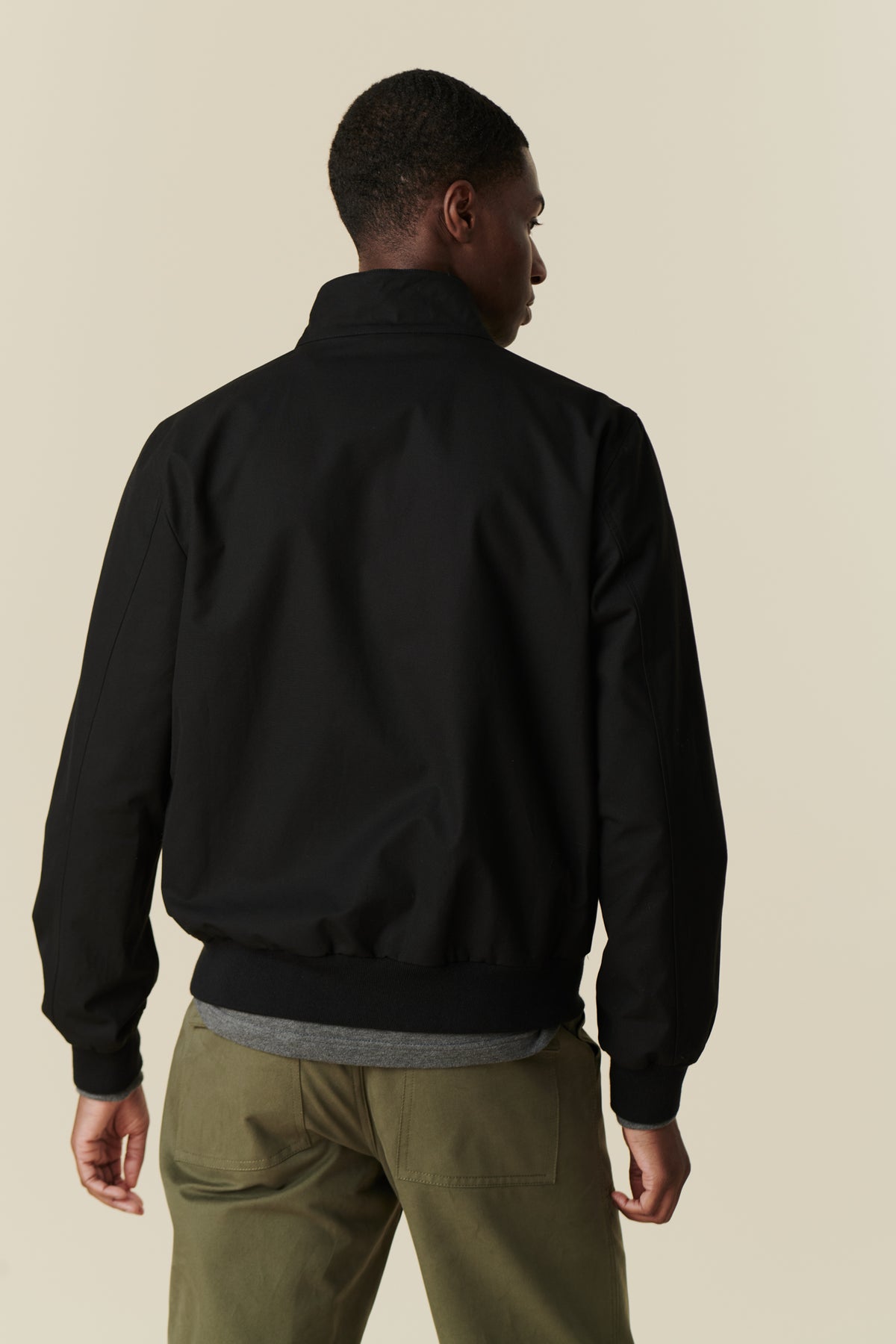 
            Back of black male wearing black Harrington jacket paired with olive combat trousers.