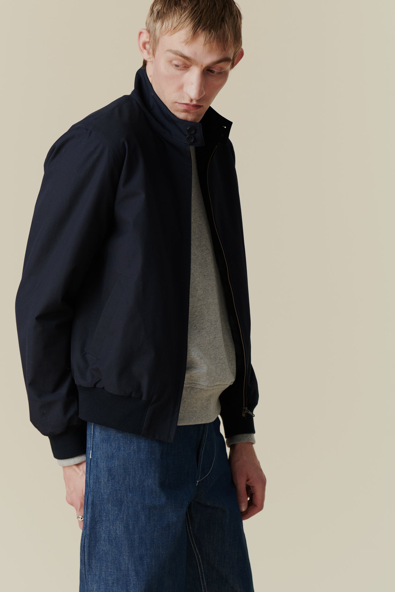 Side shot of blonde, white male wearing men's Harrington jacket in navy worn over grey raglan sweatshirt