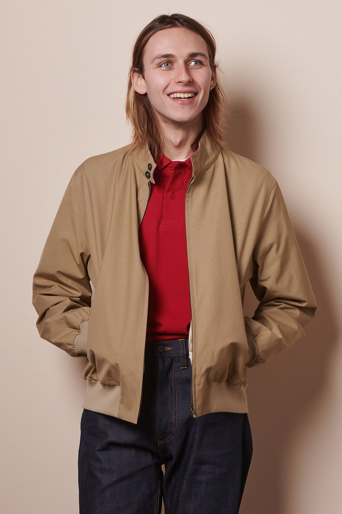 Smiley male wearing Harrington jacket unzipped with hands in pockets.