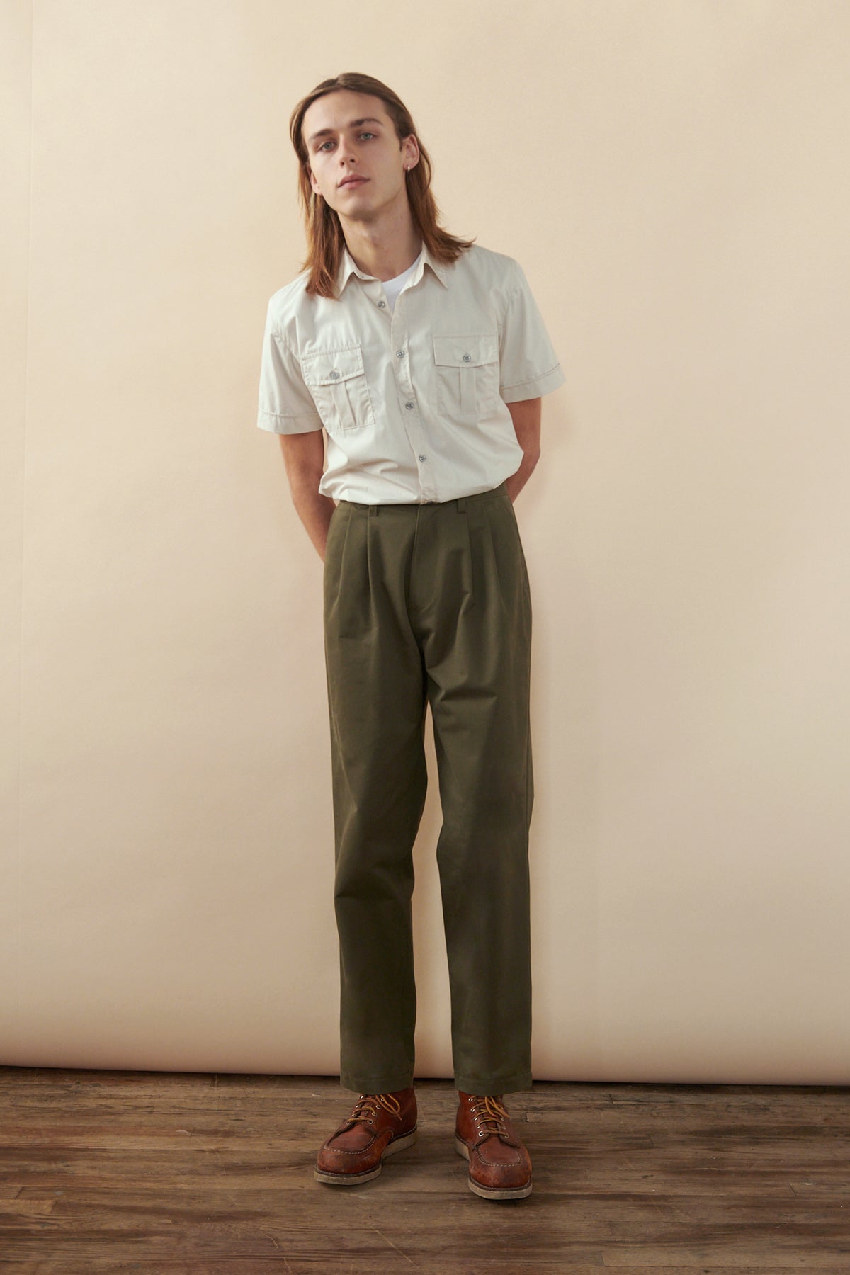 Male with shoulder length brown hair wearing Men's Heavyweight Pleated Chino in olive paired with pale military shirt
