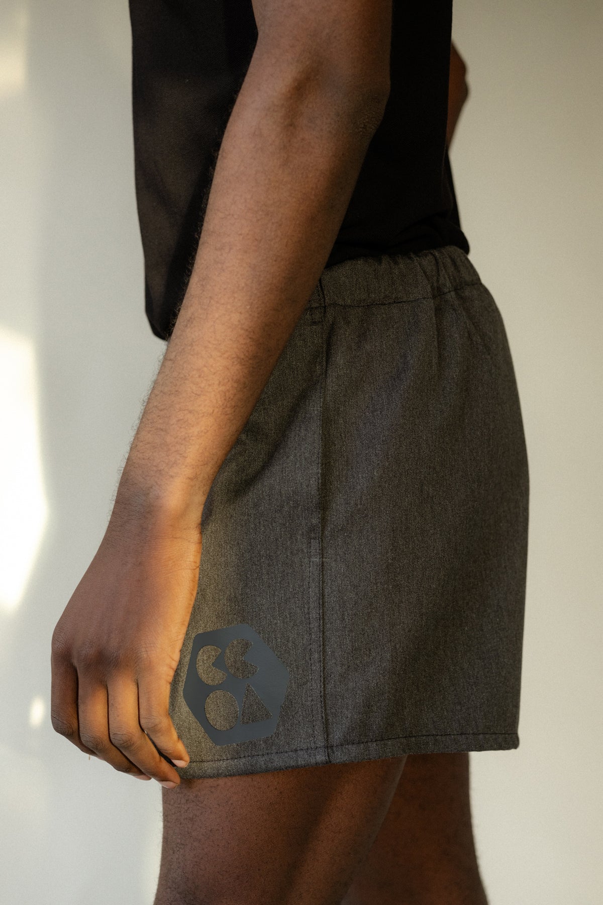 Side of male wearing men's heavyweight sports short plastic free in charcoal marl showing CCOA logo and pocket opening and elasticated waist.