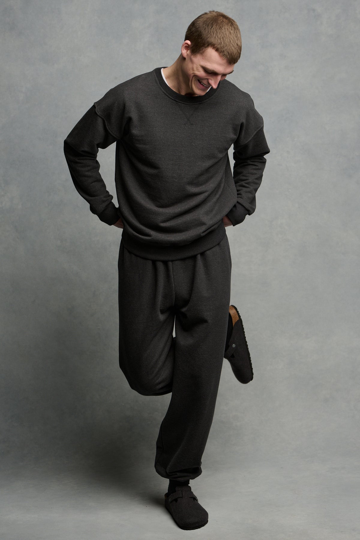 
            Full body image of smiley male looking down to ground wearing matching heritage sweatpants and sweatshirt