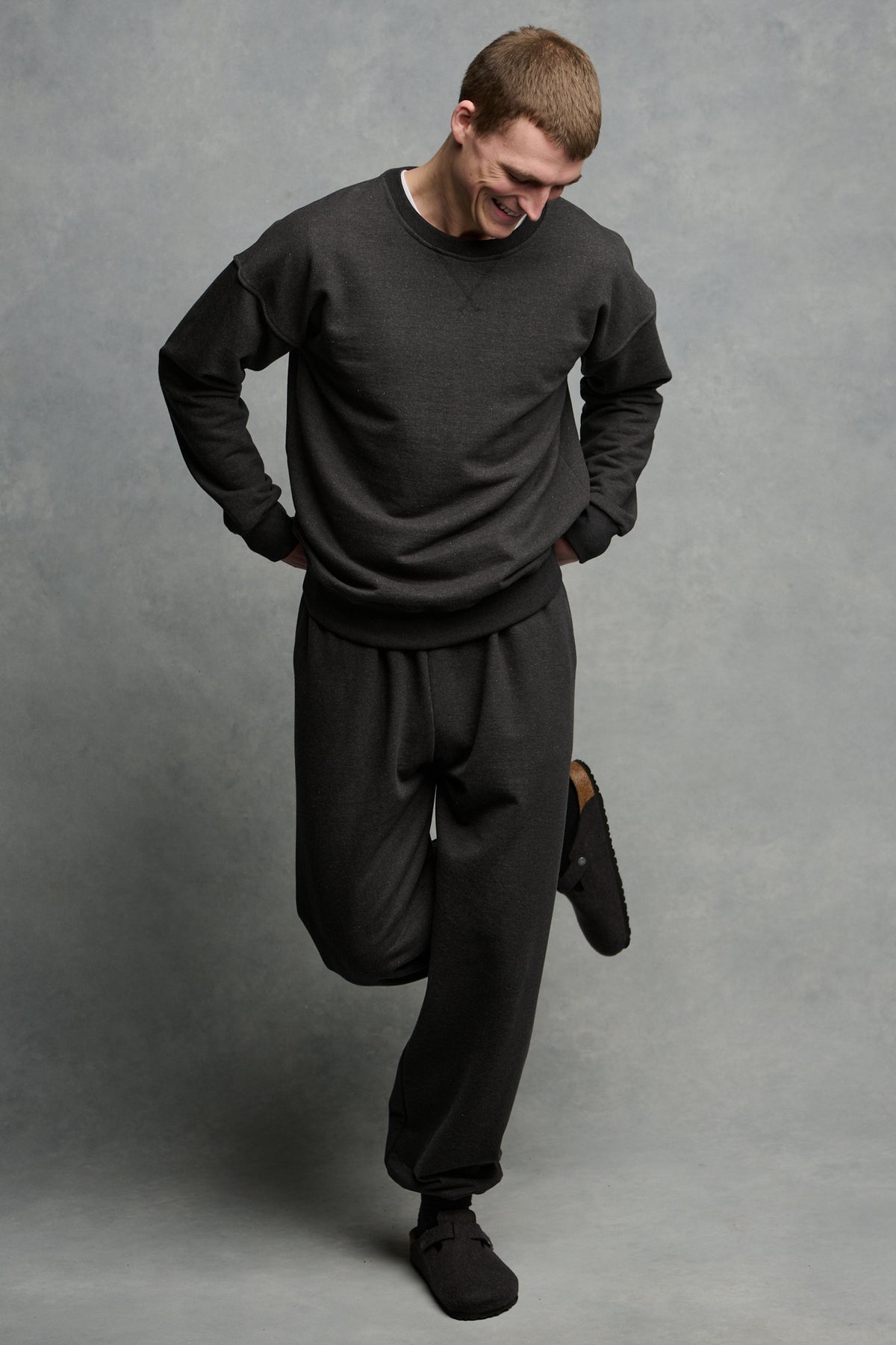 Full body image of smiley male looking down to ground wearing matching heritage sweatpants and sweatshirt