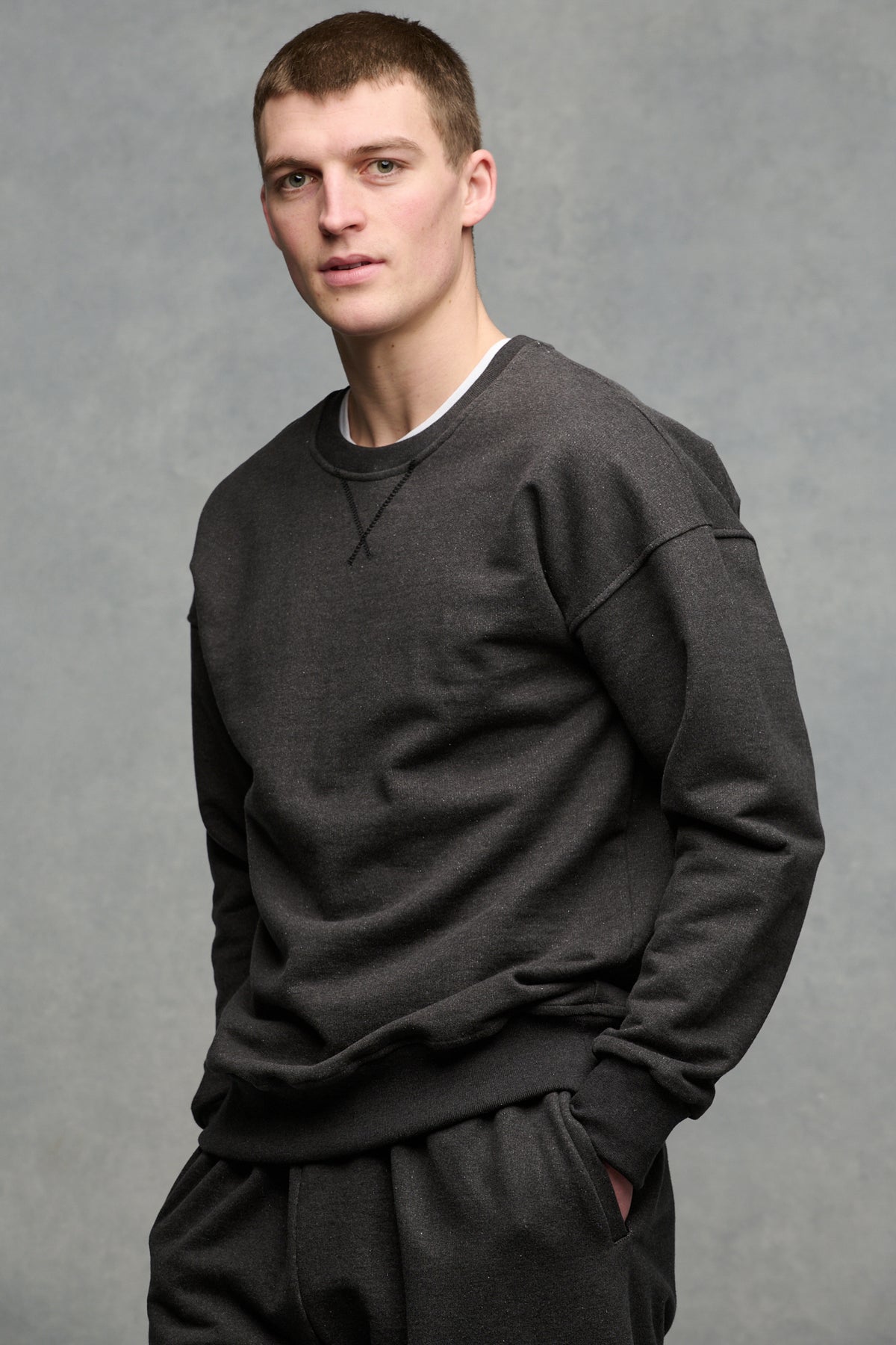 Thigh up image of male wearing heritage sweatshirt in charcoal worn over crew neck t-shirt in white paired with matching heritage sweatpants in charcoal