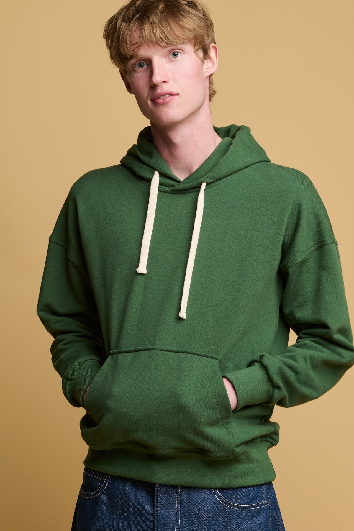 Thigh up image of male with his hands in the pocket of hooded sweatshirt in bottle green