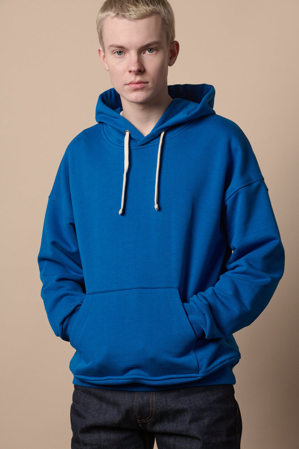
            Male wearing cobalt hooded sweatshirt with hands in front pocket, worn with indigo jeans