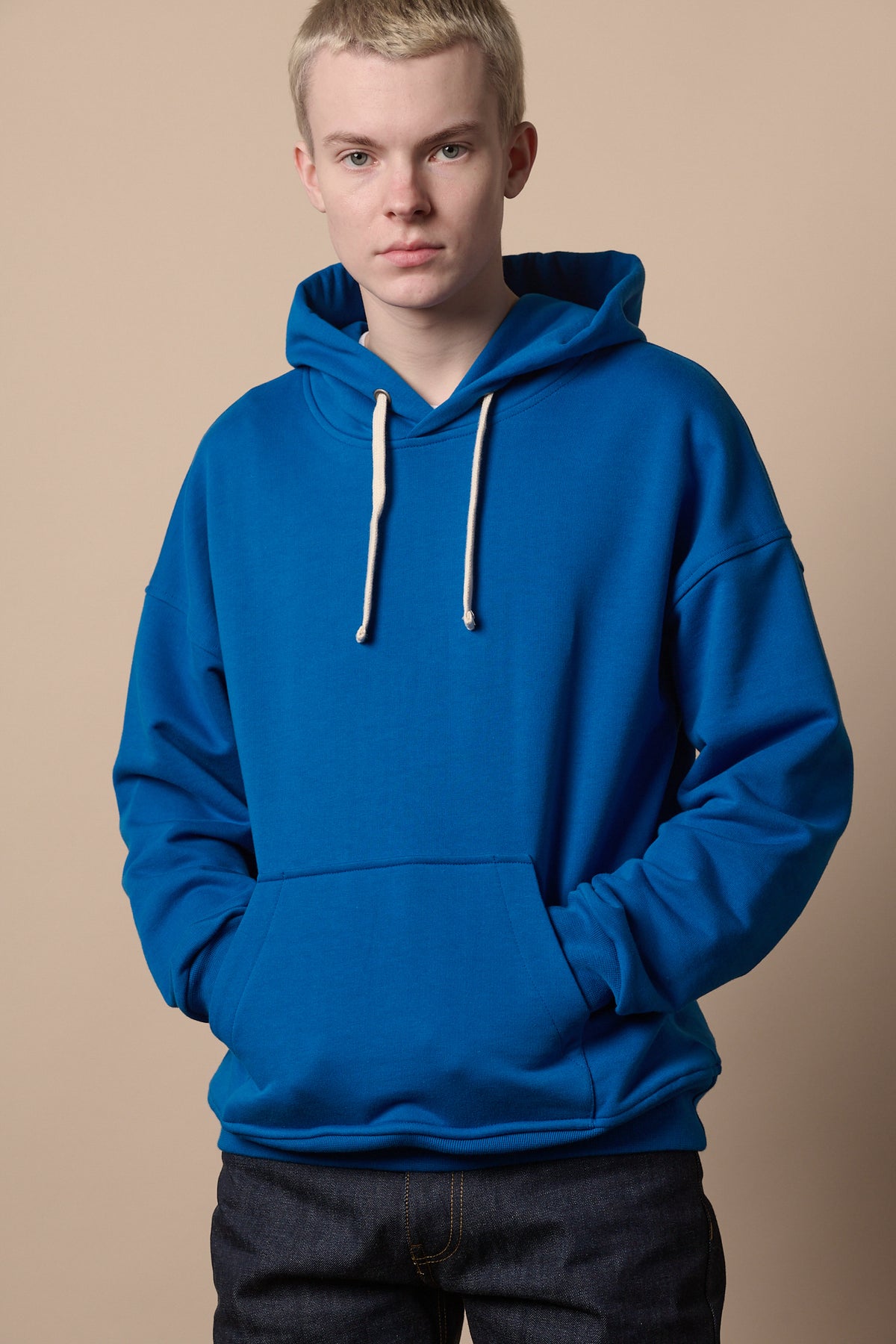 Male wearing cobalt hooded sweatshirt with hands in front pocket, worn with indigo jeans