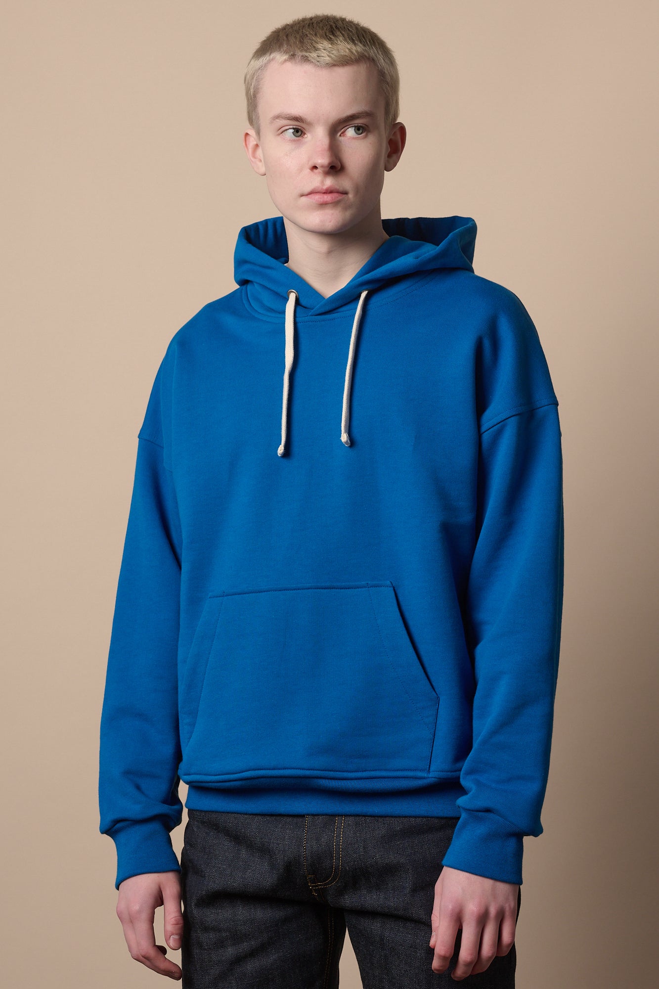 Thigh up image of blonde male wearing cobalt hooded sweatshirt 