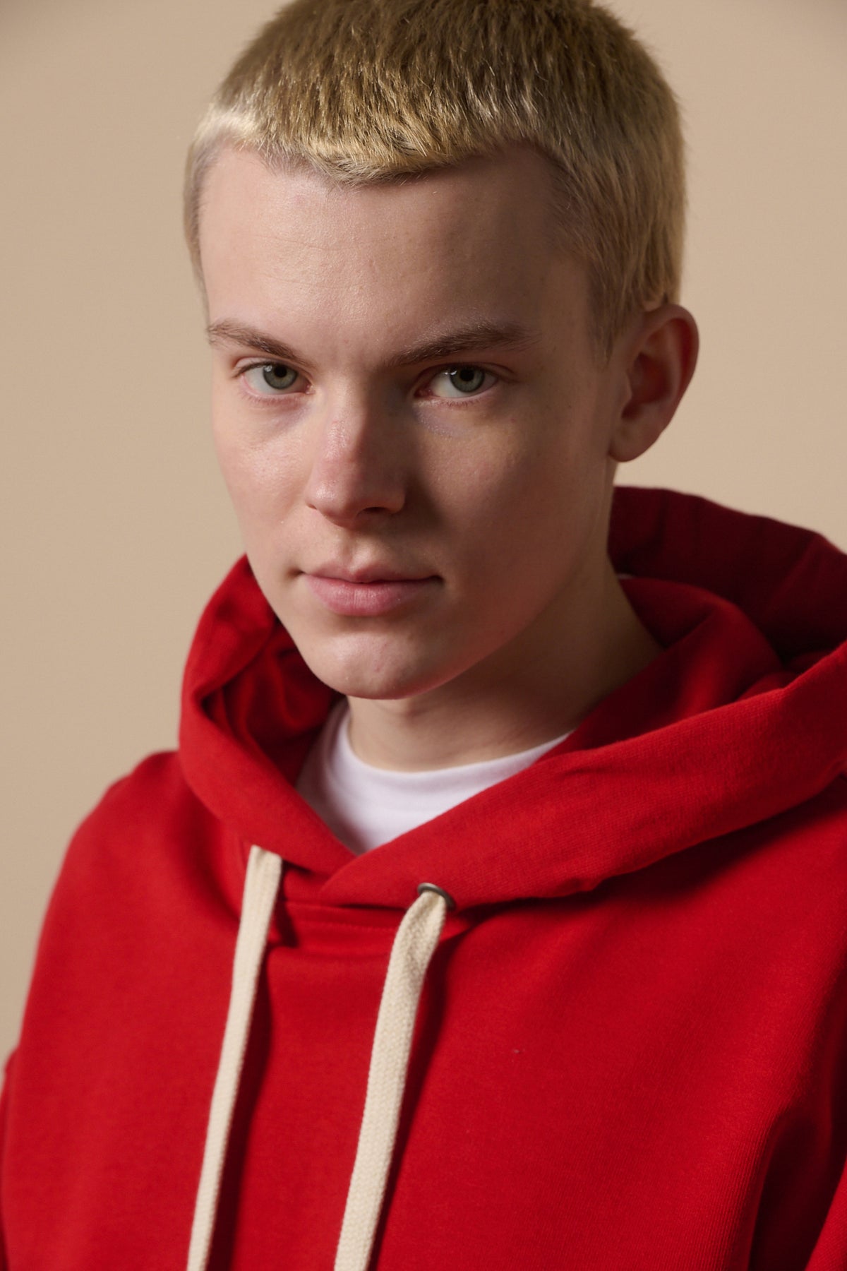 
            Portrait of white male wearing hooded sweatshirt in crimson worn over white t shirt. Ecru draw cord through hood.