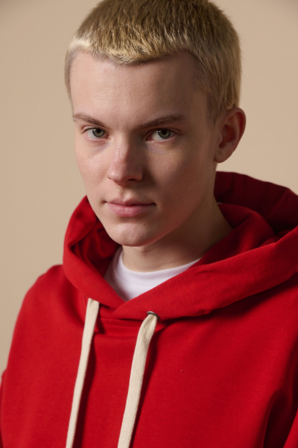 Portrait of white male wearing hooded sweatshirt in crimson worn over white t shirt. Ecru draw cord through hood.