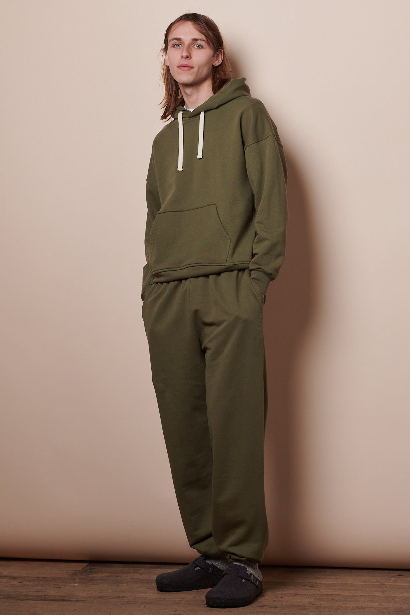 Full body image of male wearing hooded sweatshirt in olive paired with matching sweatpants 