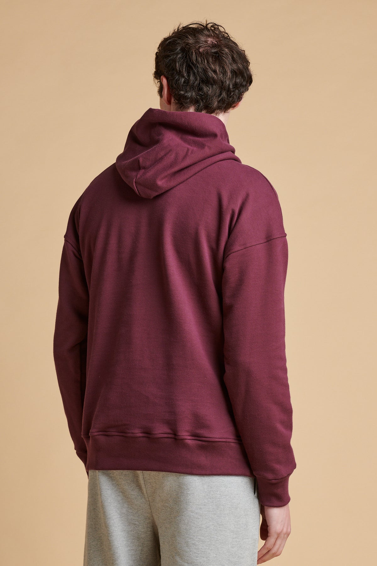 Thigh up of the back of male wearing hooded sweatshirt in plum.