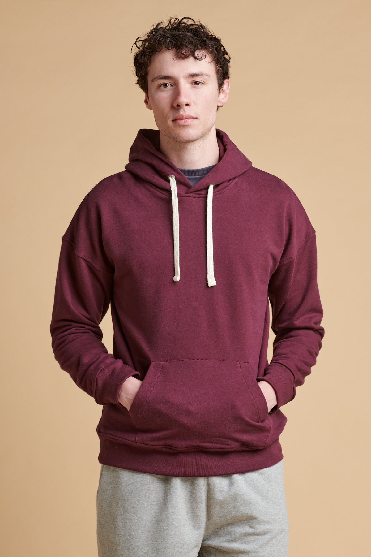 Thigh up of male wearing hooded sweatshirt in plum.