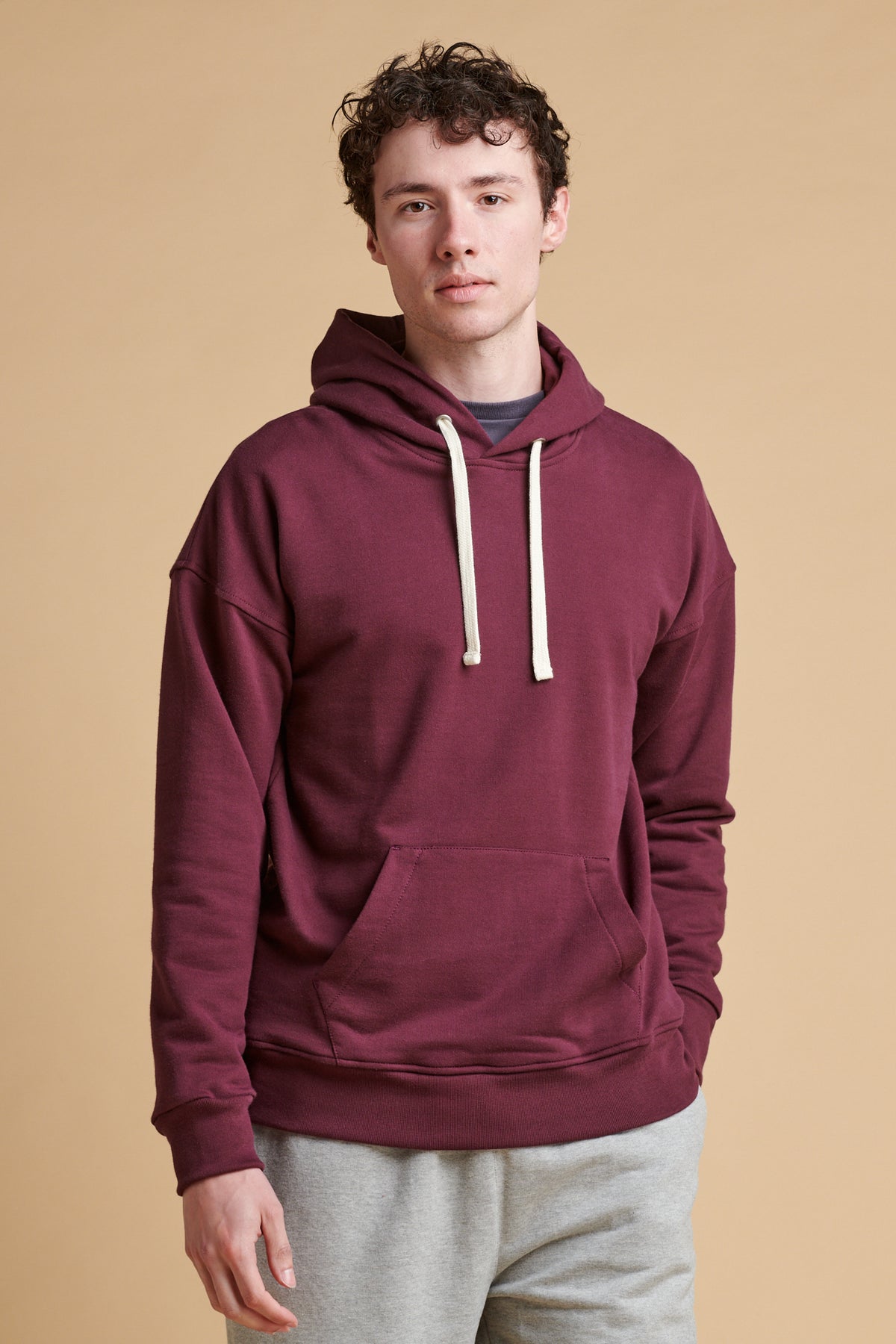 Thigh up of male wearing hooded sweatshirt in plum.