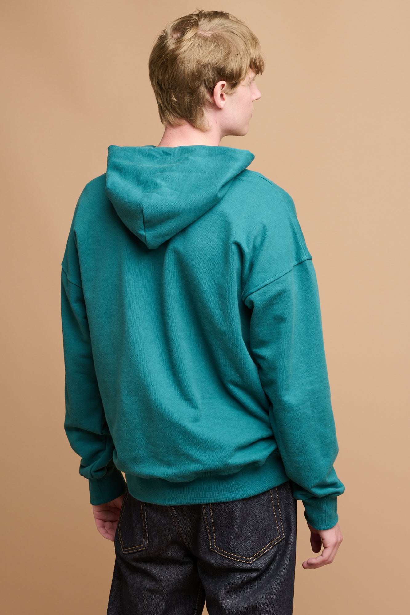 Close up head shot of smiley male with blonde hair wearing hooded sweatshirt in teal over white crew neck t shirt