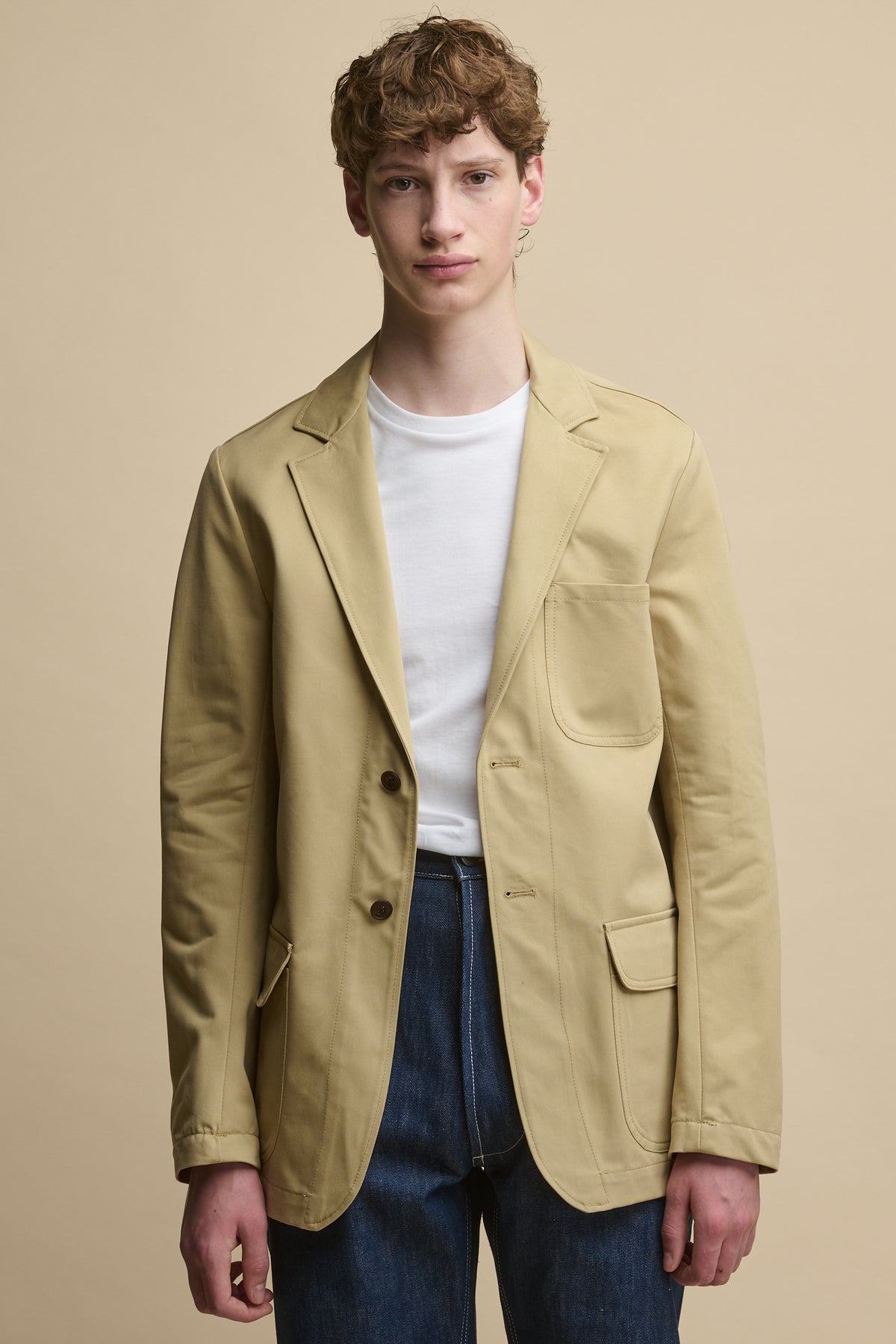 Thigh up image of Men's James Single Breasted Blazer in stone worn over short sleeve t shirt in white with chore jeans in blue