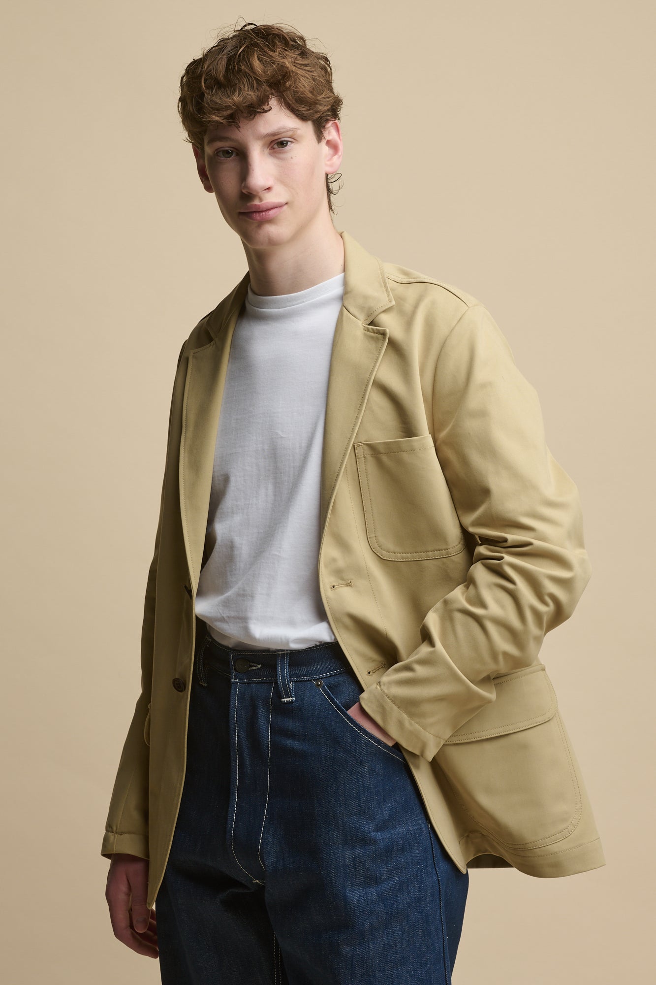 Thigh up image of male wearing Men's James Single Breasted Blazer in stone over a short sleeve t shirt in white with chore jeans in blue