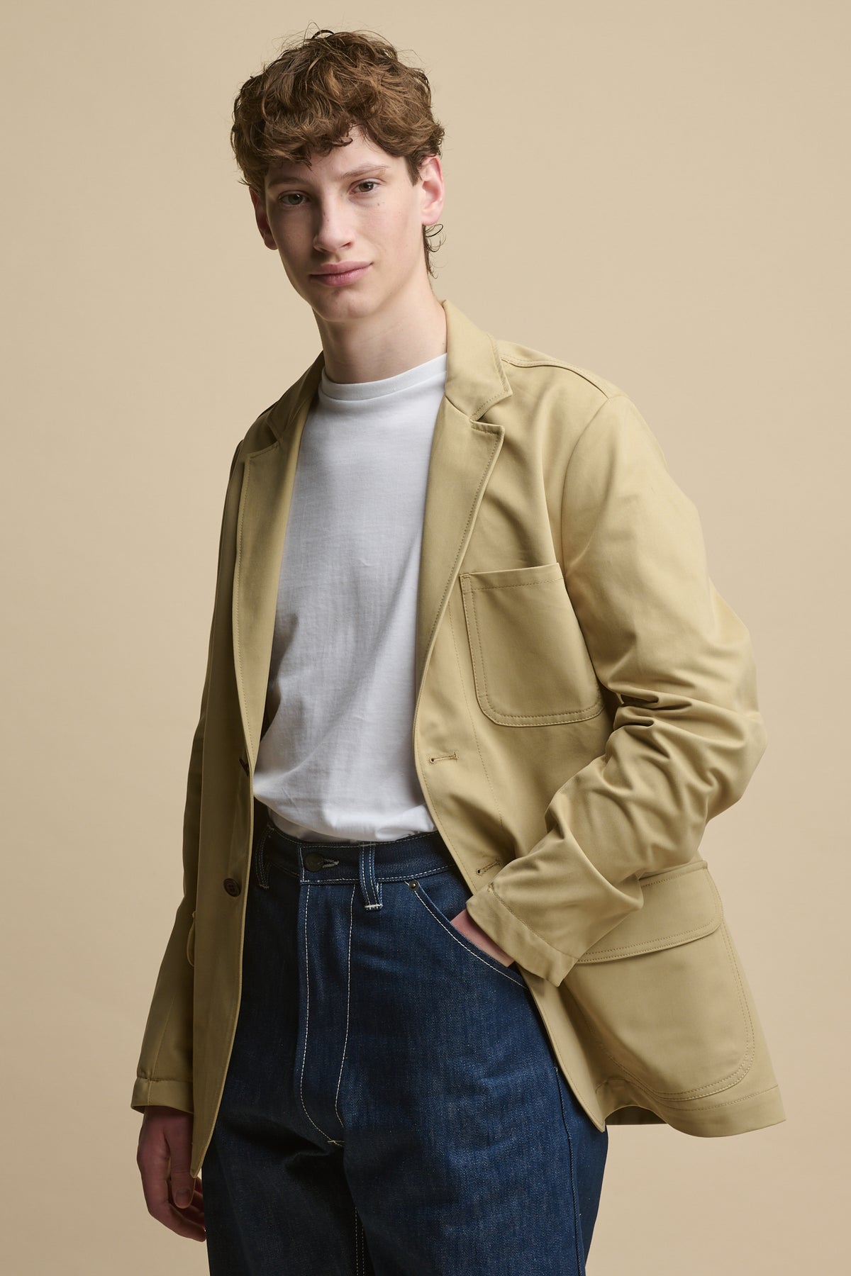 Thigh up image of male wearing Men's James Single Breasted Blazer in stone over a short sleeve t shirt in white with chore jeans in blue