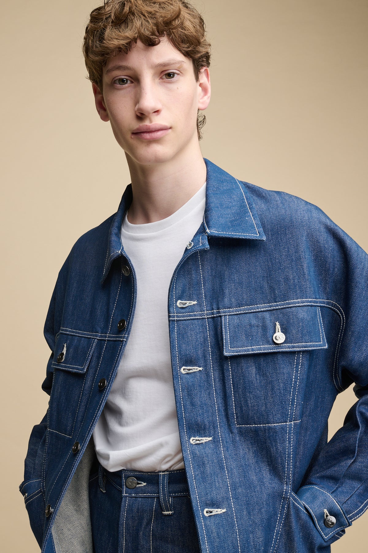 Waist up image of male wearing joe Denim Jacket in blue with his hands in two front pockets