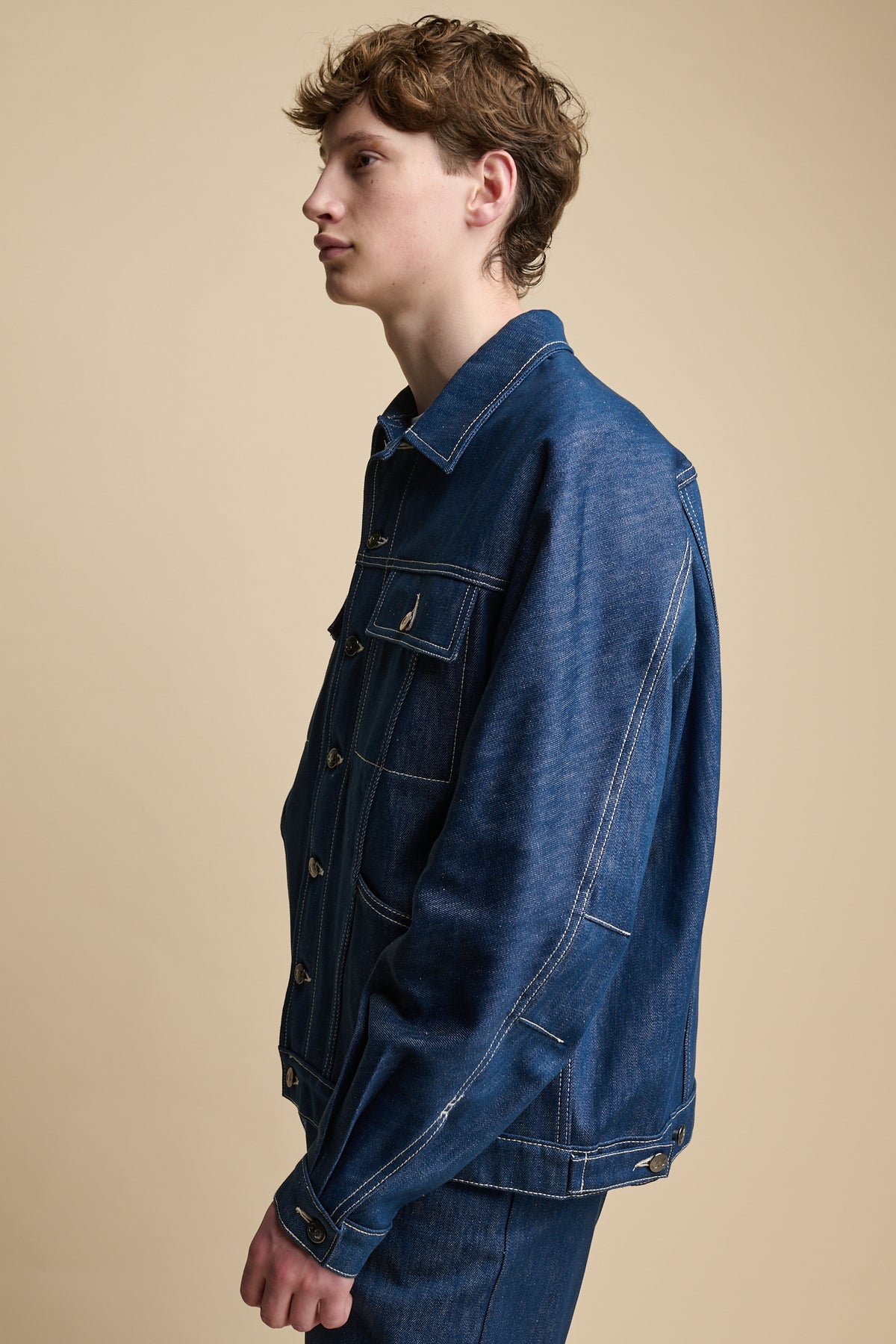 Thigh up image of the side of male wearing Joe Denim Jacket in blue, cuff with button fastening.