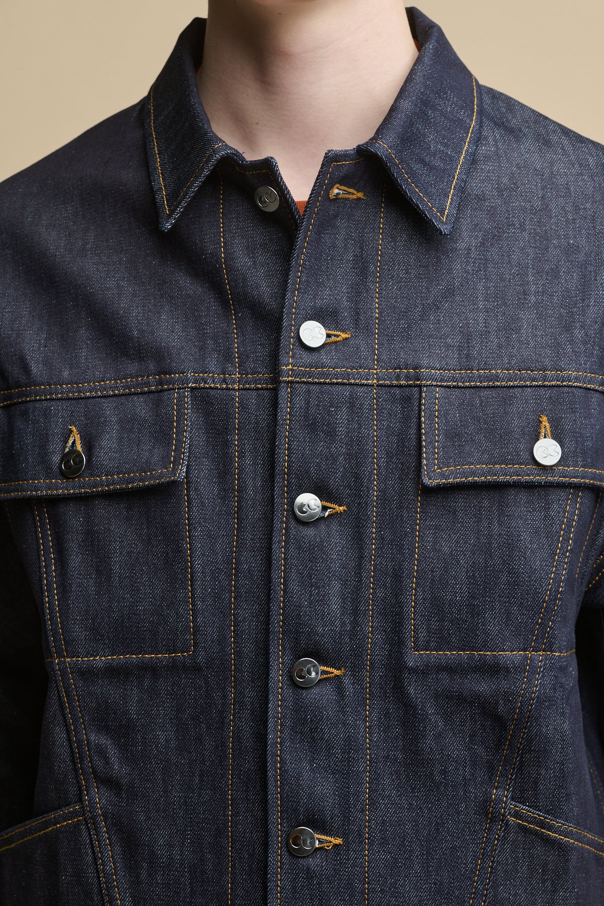 Detail shot of the front of Joe Denim Jacket in indigo, two front chest pockets with flap and button fastenings, CC logo branded buttons