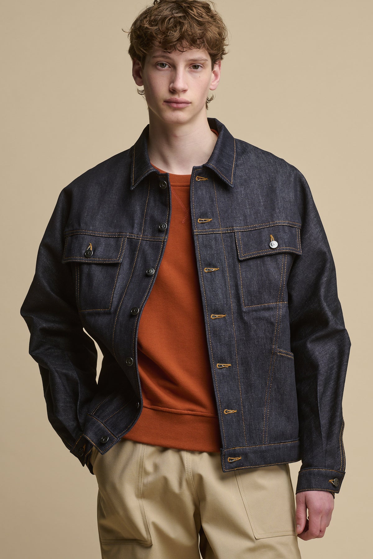Thigh up image of the front of male wearing joe denim jacket in indigo worn over cinnamon raglan sweatshirt