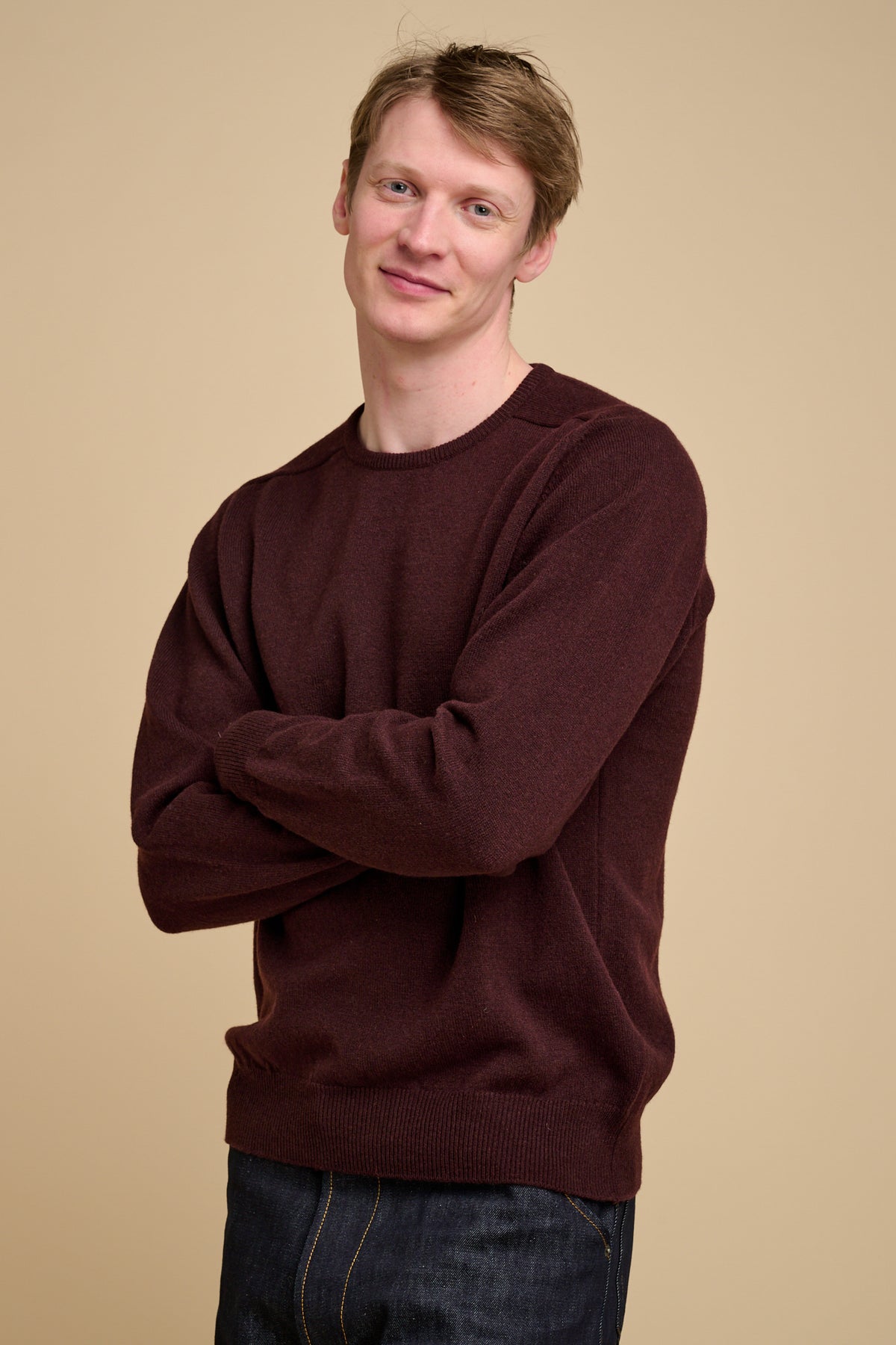 Man wearing a chocolate lambswool crew neck jumper against a beige background.