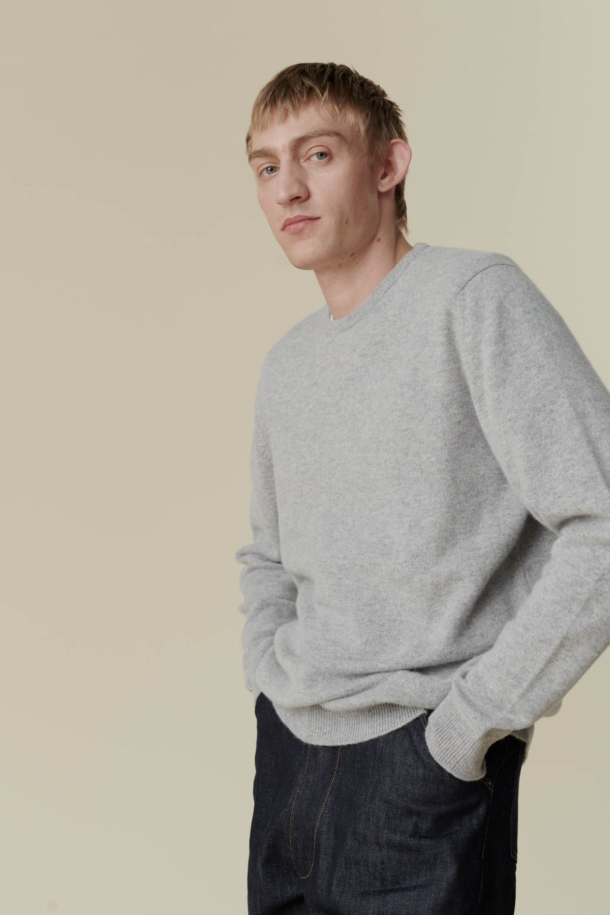 
            Image showing above thigh of white male wearing men&#39;s lambswool crew neck in light grey with his hands in the pockets of men&#39;s Indigo chore jean
