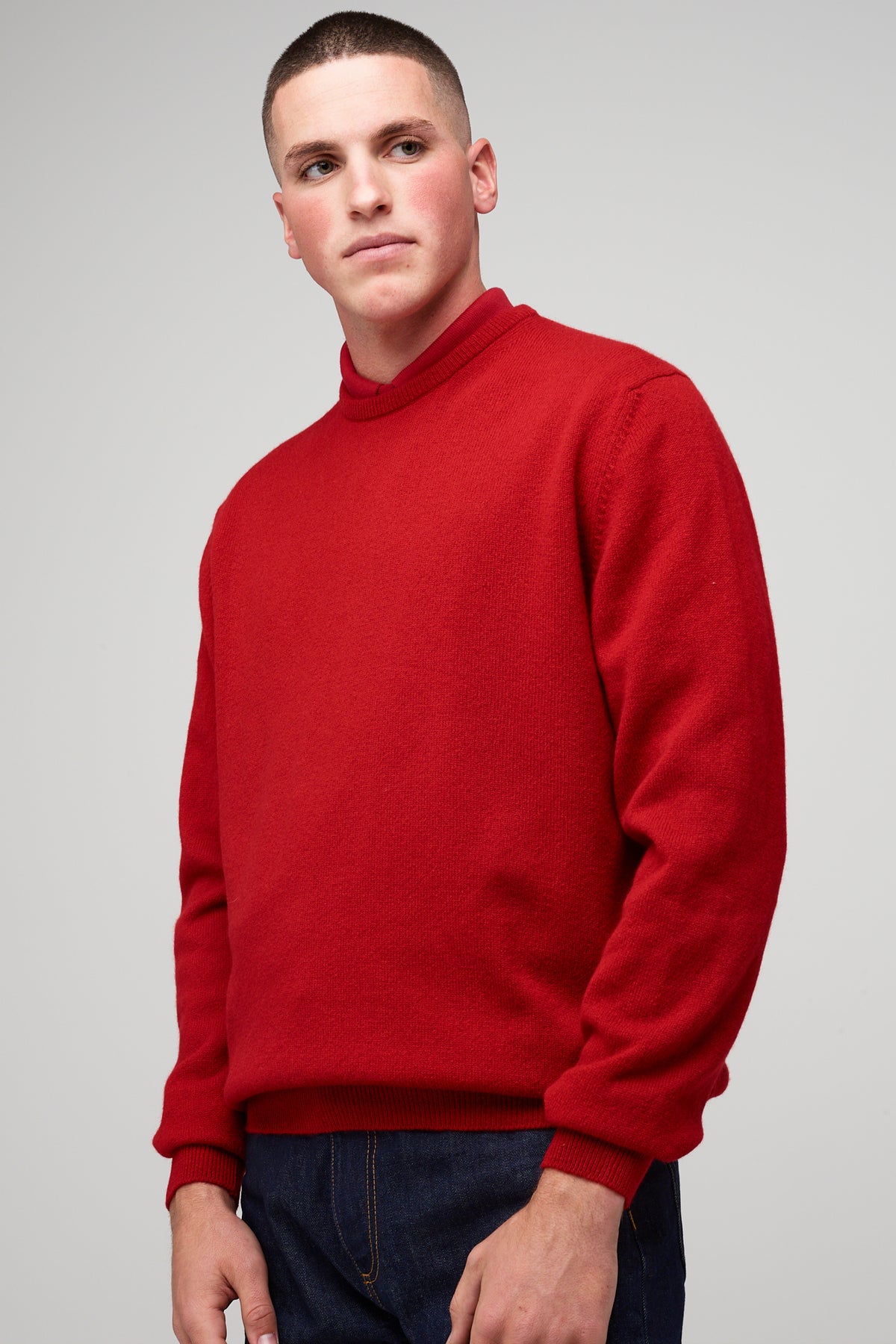 Brunette, white male wearing men's Lambswool Crew Neck in red styled with denim jean