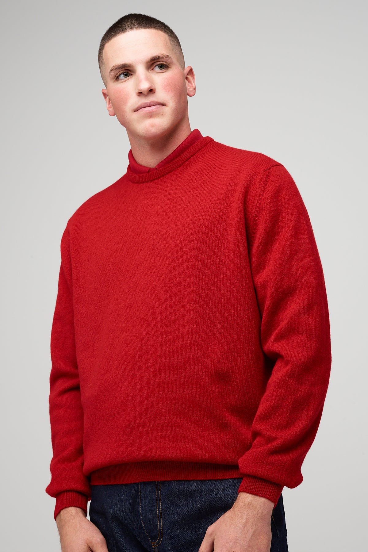 Brunette, white male wearing men's Lambswool Crew Neck in red styled with denim jean