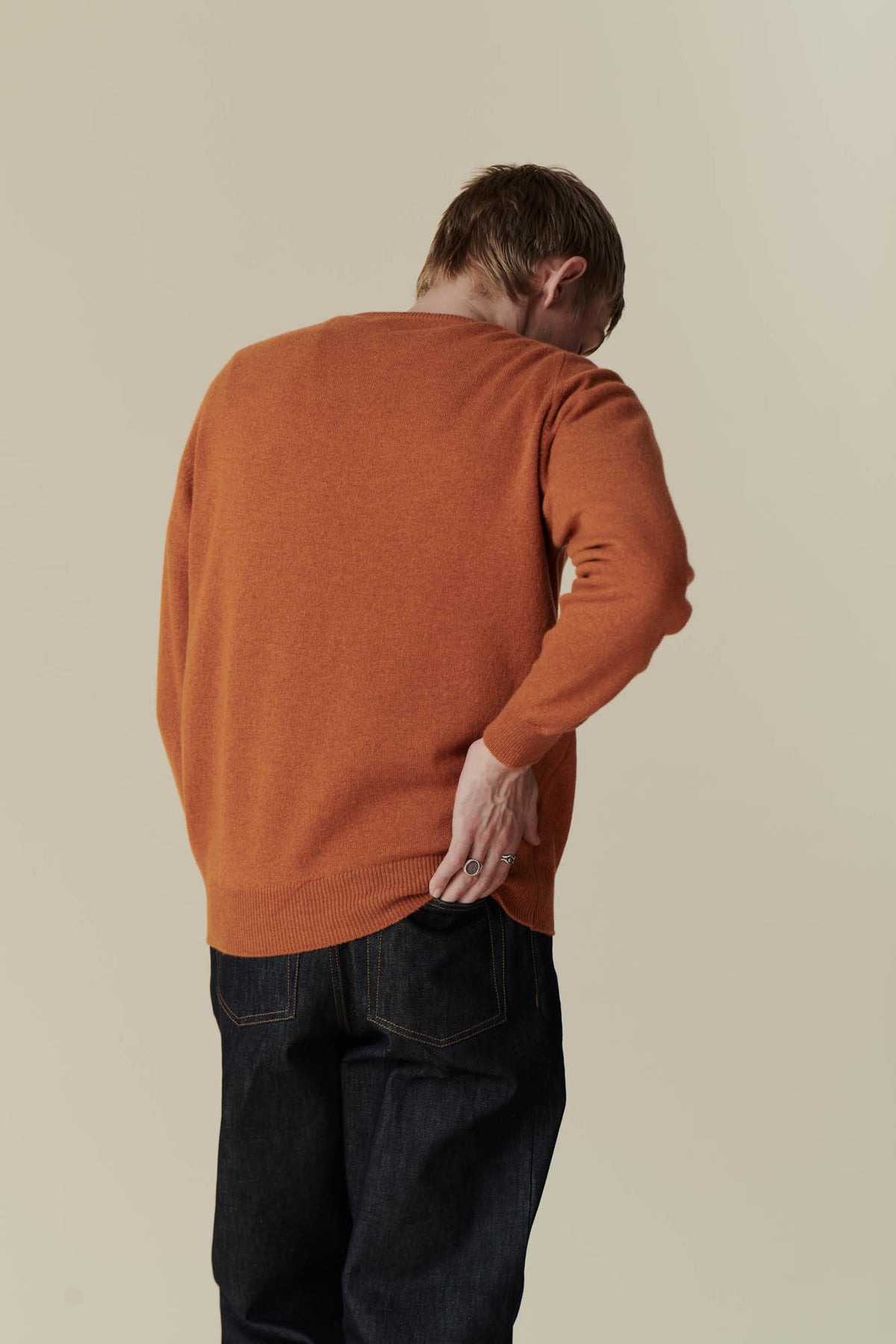 
            Thigh up image of back of white male wearing men&#39;s lambswool saddle shoulder crew neck in rust.