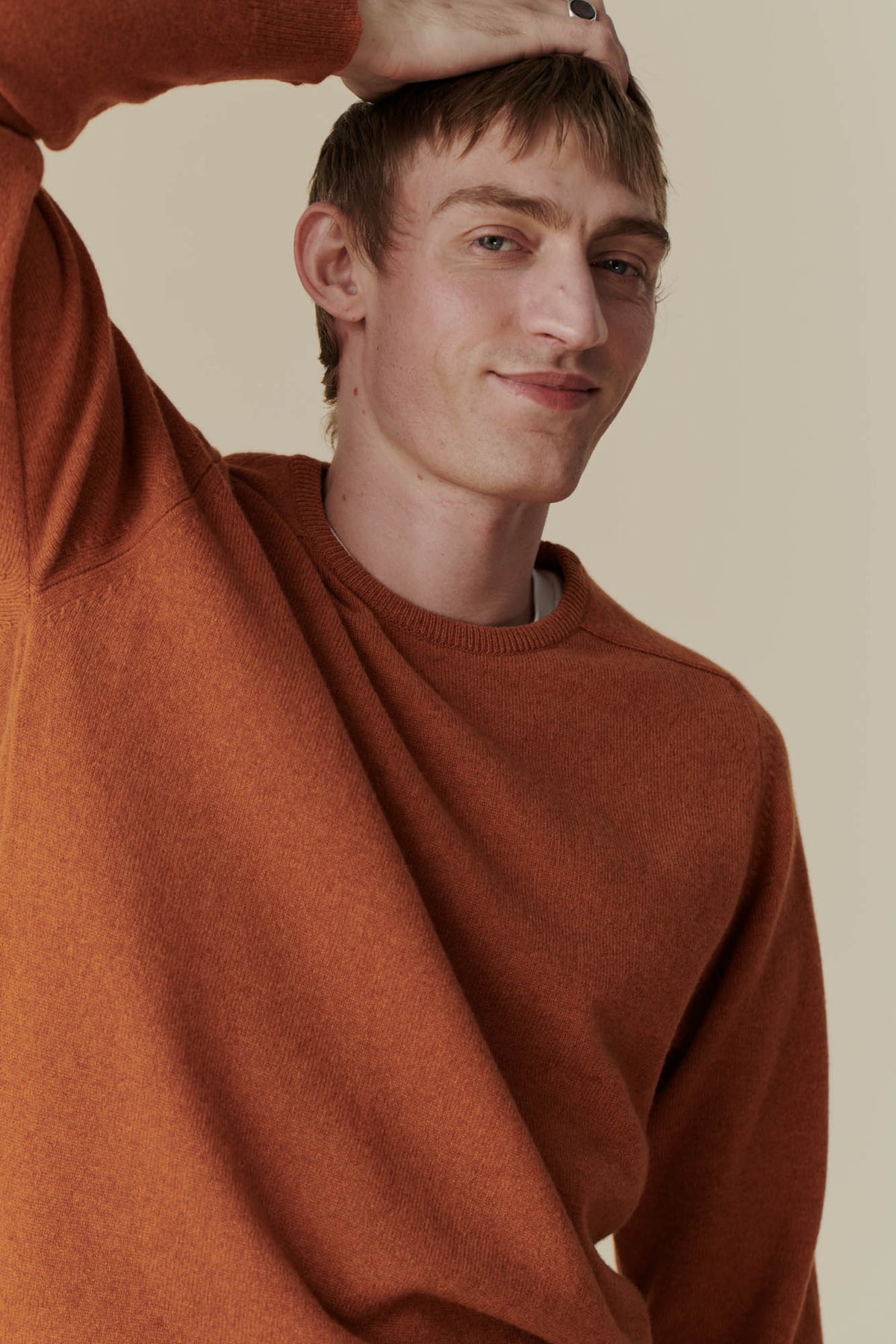 
            Waist up shot of white male with hand on head, wearing men&#39;s lambswool saddle shoulder crew neck in rust
