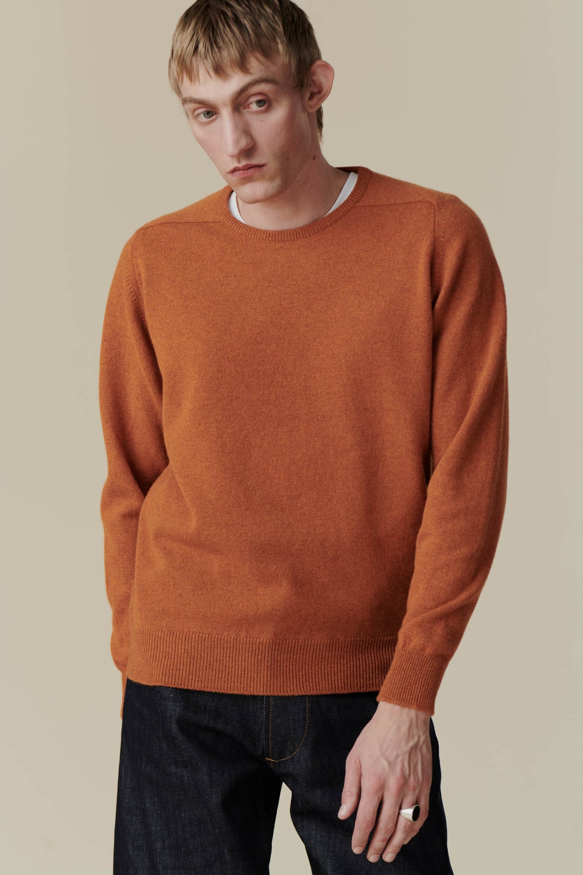 
            Thigh up image of dirty blonde, white male wearing lambswool saddle shoulder crew neck in rust