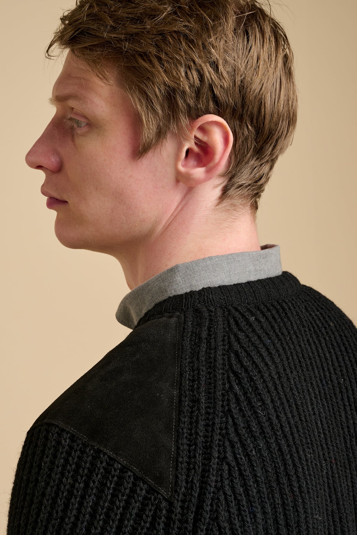 The back of man wearing black ribbed knit jumper against a beige background