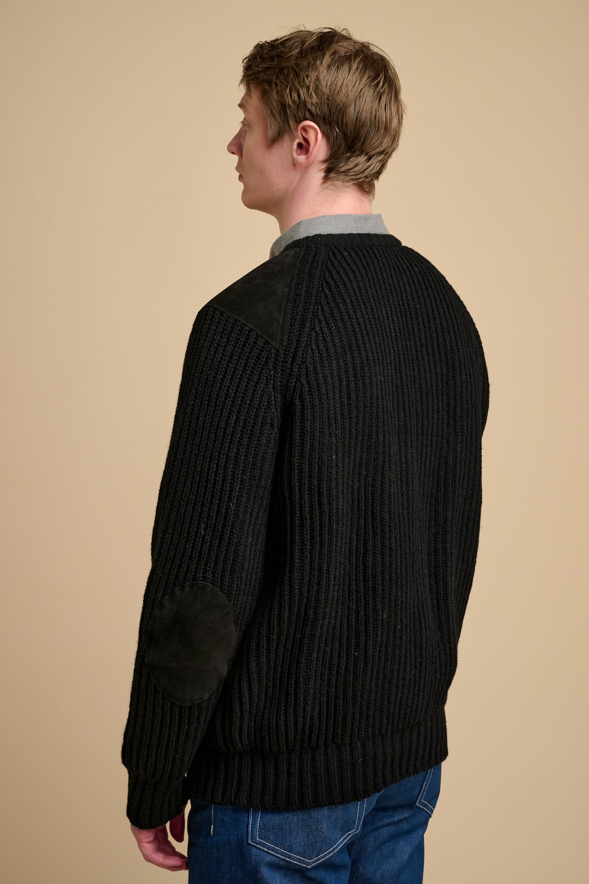 Man wearing a black ribbed sweater against a beige background