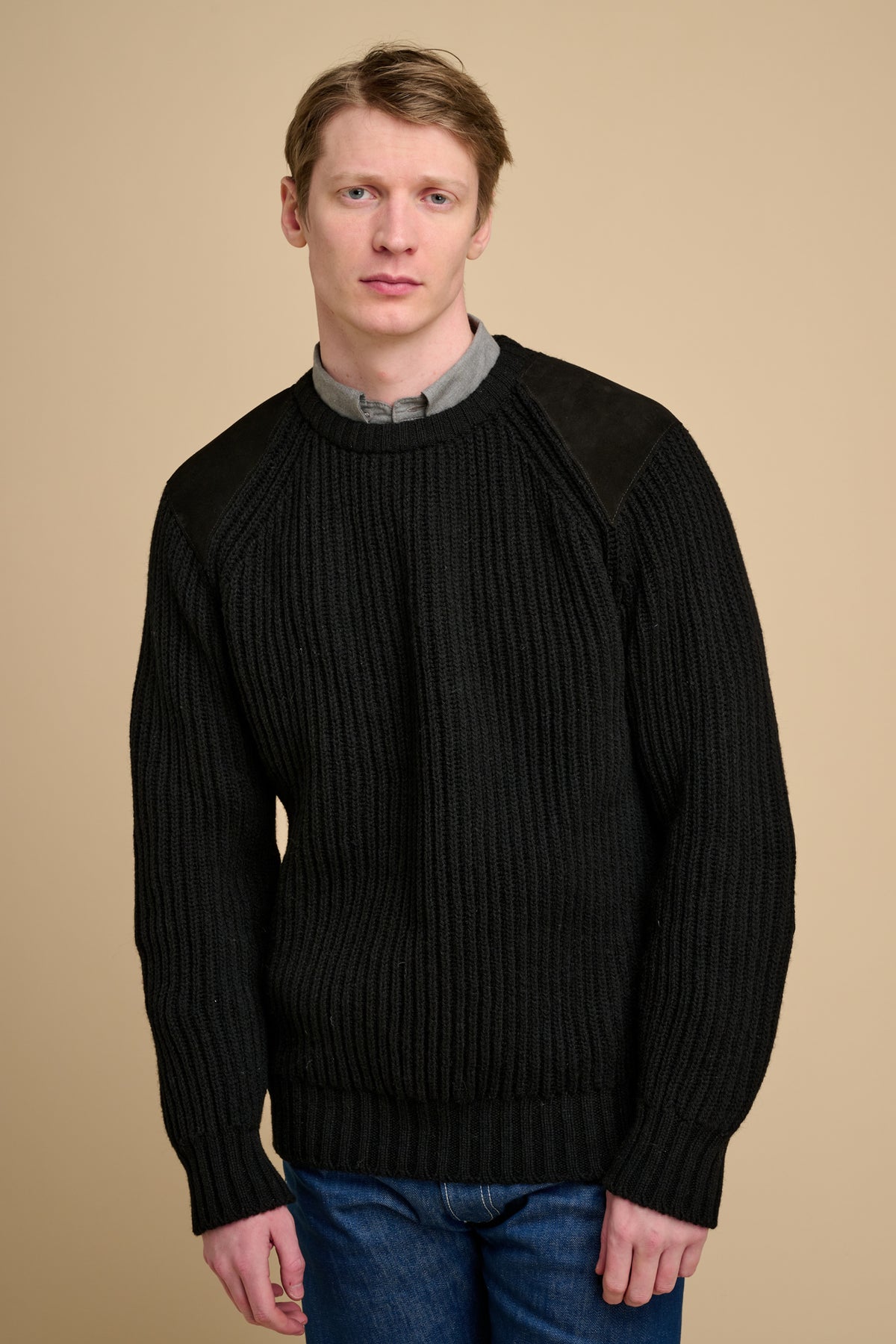 Man wearing a black sweater against a beige background.