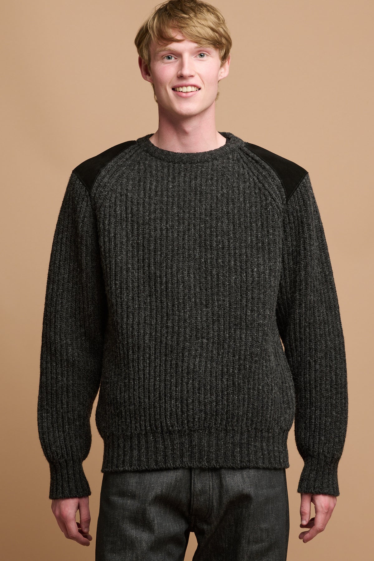The front of male thigh up wearing lambswool fisherman ribbed jumper in charcoal with suede shoulder patches