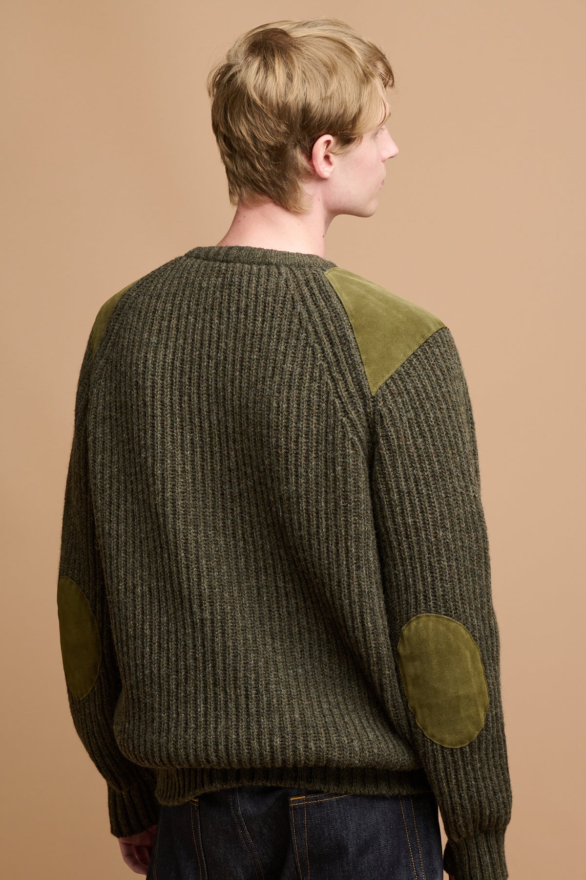 The back of male wearing lambswool fisherman ribbed jumper in dark olive with suede patches on the shoulder and elbow