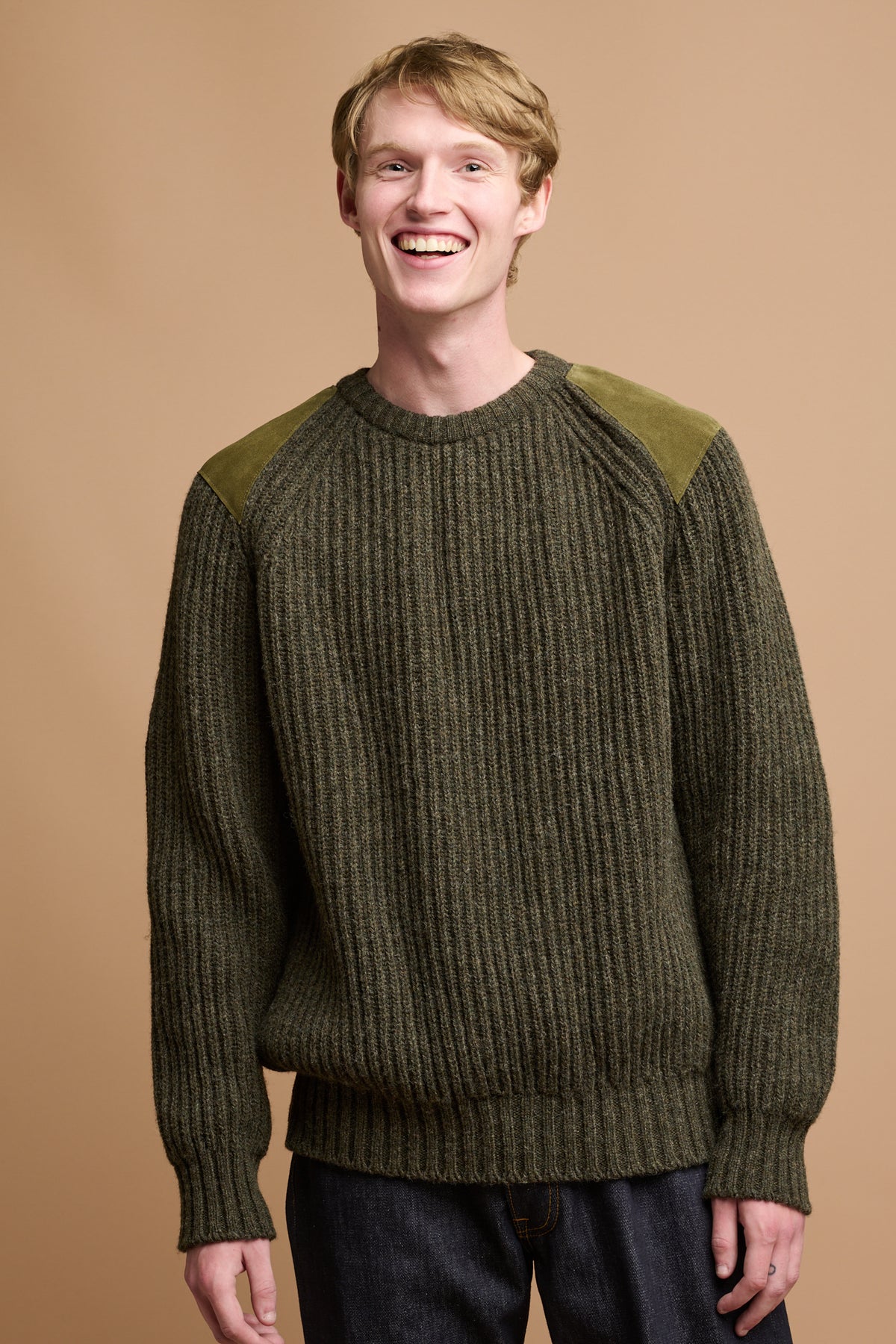 Thigh up image of smiley male with blonde hair wearing lambswool fisherman ribbed jumper in dark live