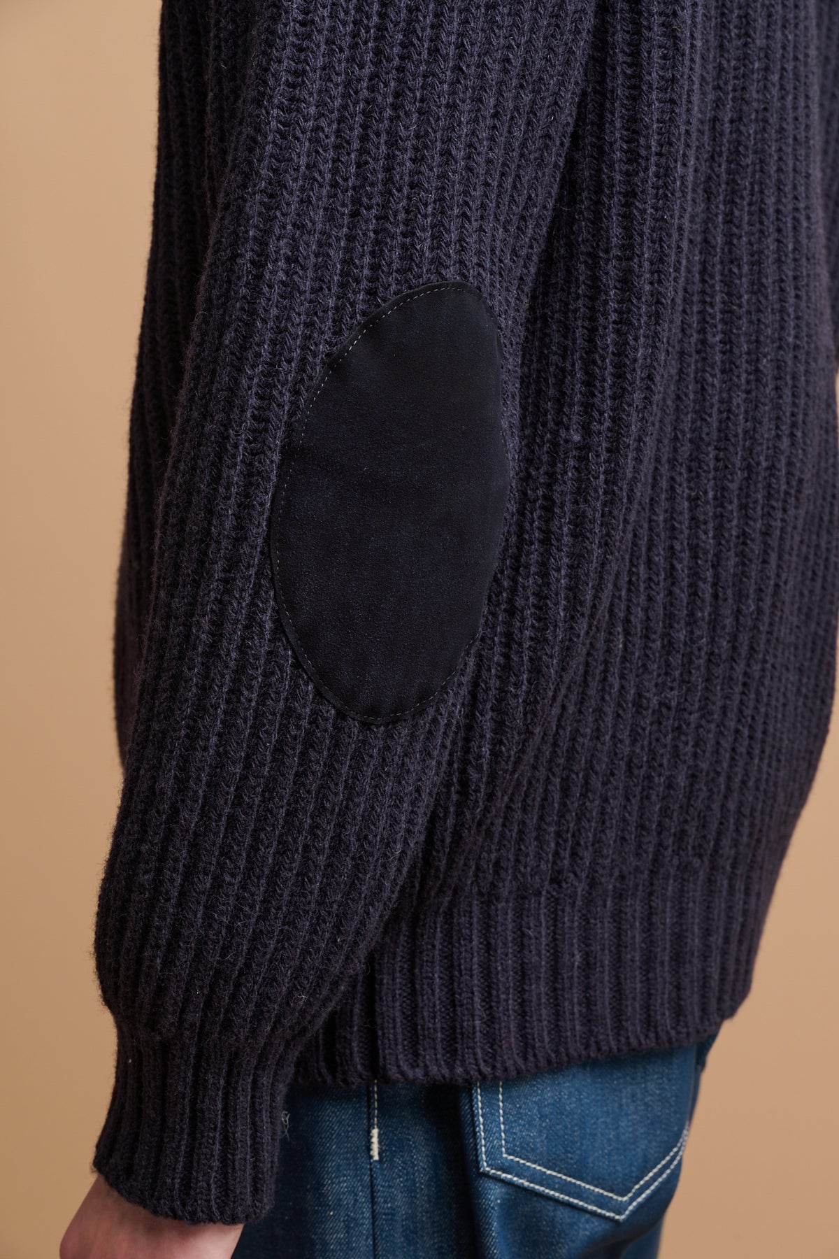 Close up detail of the suede elbow patch on the lambswool fisherman ribbed jumper in navy