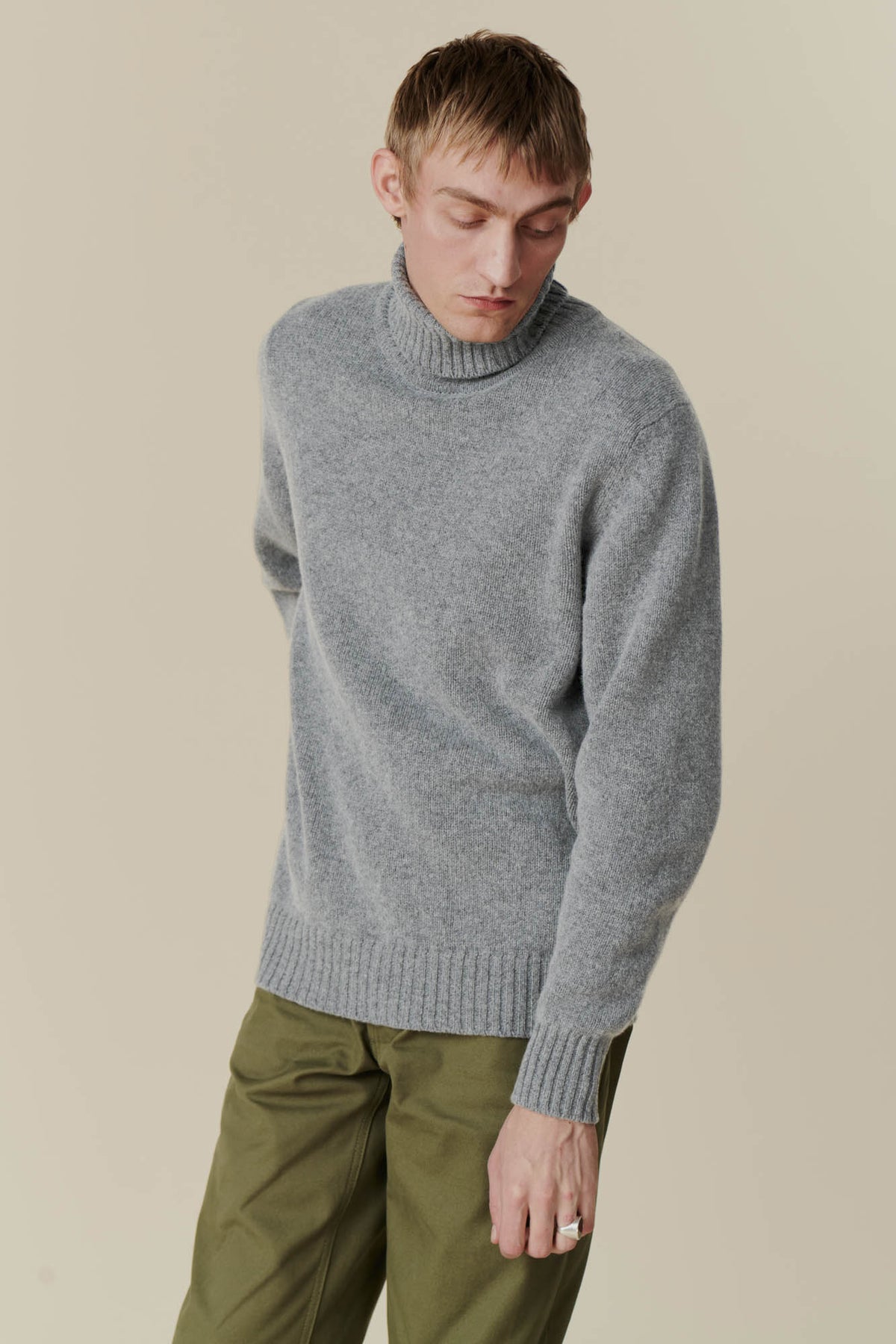 
            White male wearing men&#39;s lambswool roll neck jumper in flannel grey with cameraman pant in olive