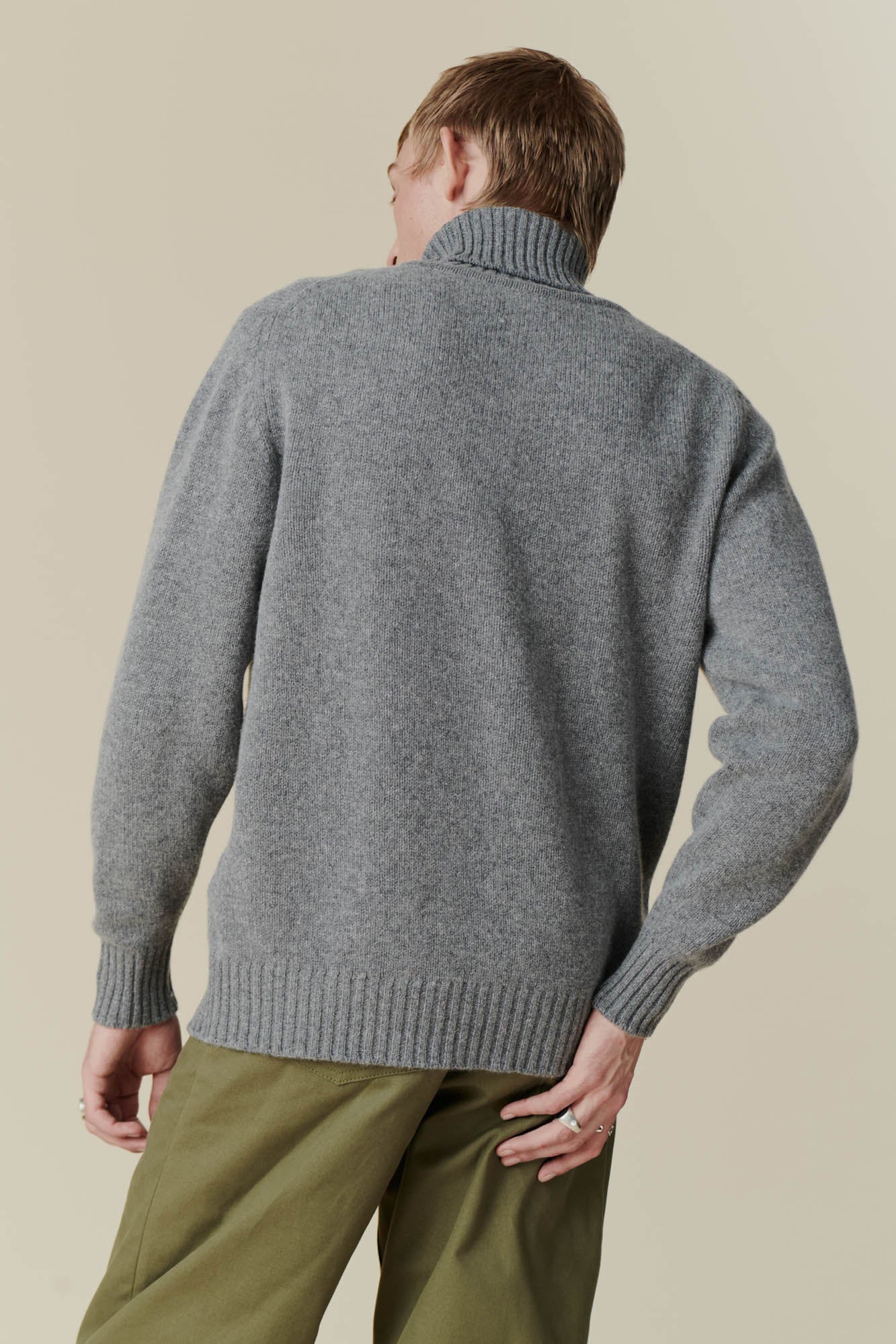 Back shot of male wearing grey roll neck jumper and olive cameraman pant