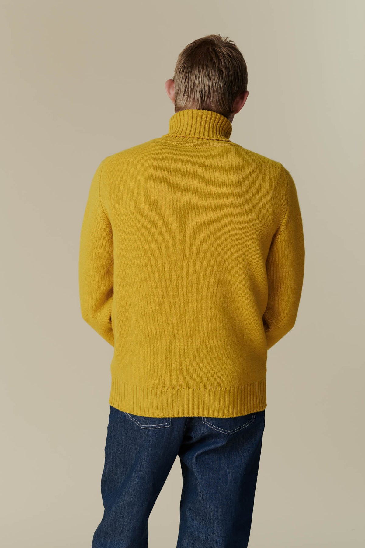 Behind shot of male in mustard lambswool roll neck.