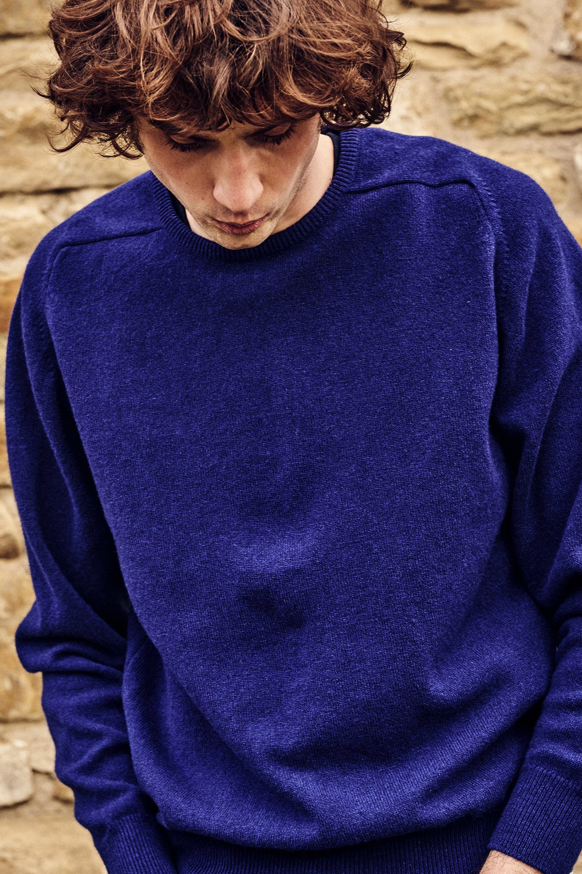 Person wearing a blue sweater against a stone wall background