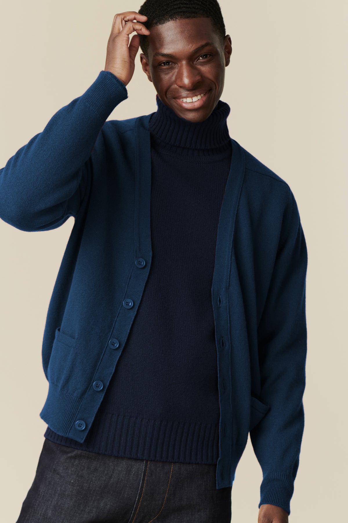 
            Smiley, black male wearing lambswool v neck cardigan in bright blue over navy roll neck