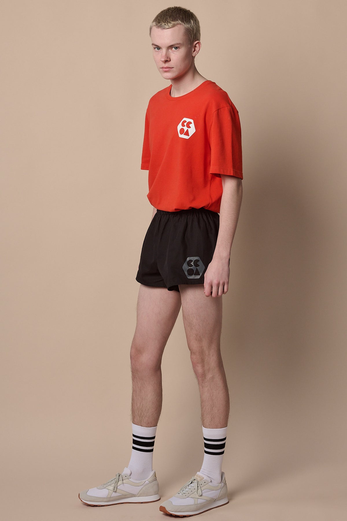 
            Full body image of white male wearing men&#39;s lightweight sports short plastic free in black with CCOA logo paired with breathable short sleeve t shirt in flame red.