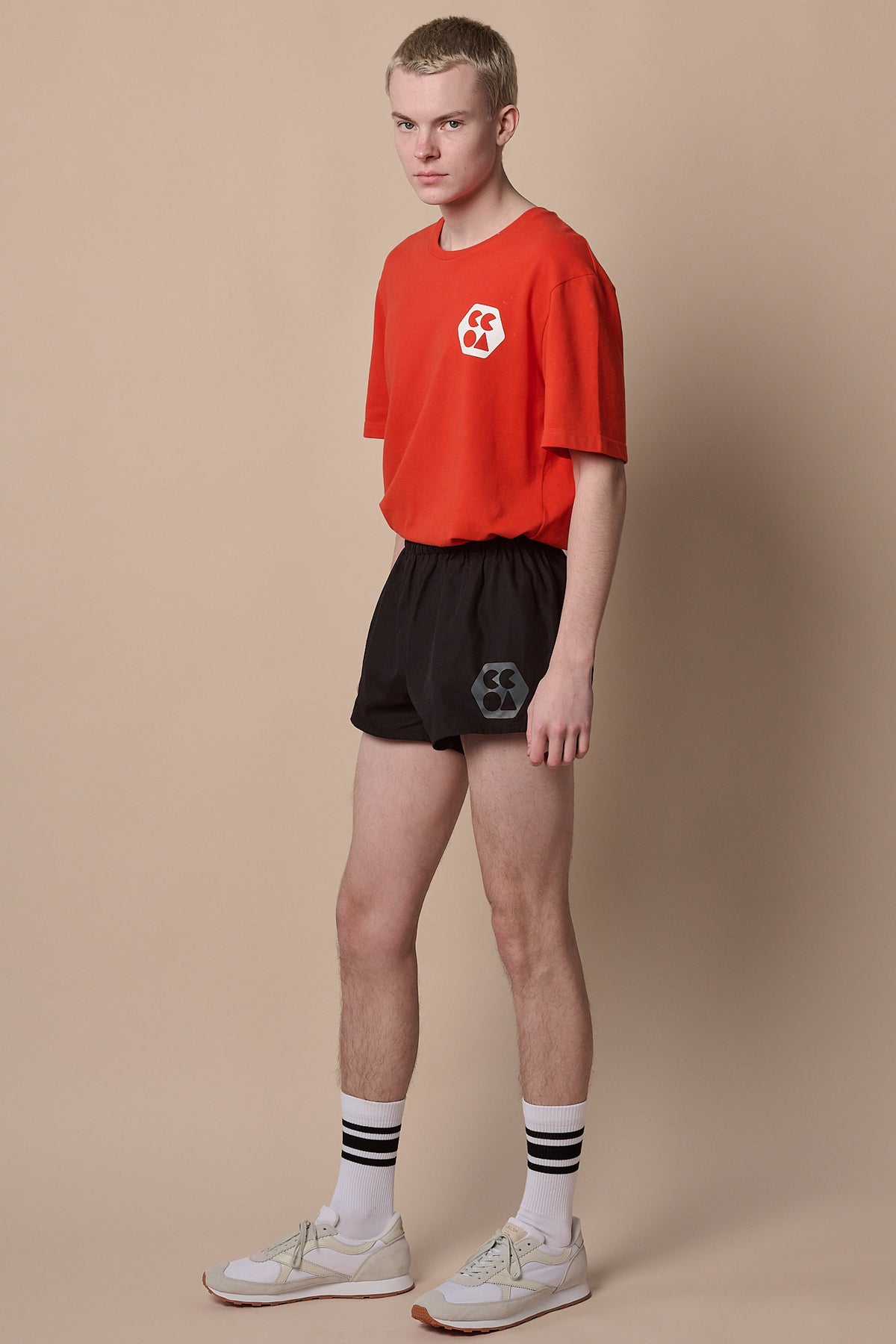 Full body image of white male wearing men's lightweight sports short plastic free in black with CCOA logo paired with breathable short sleeve t shirt in flame red.