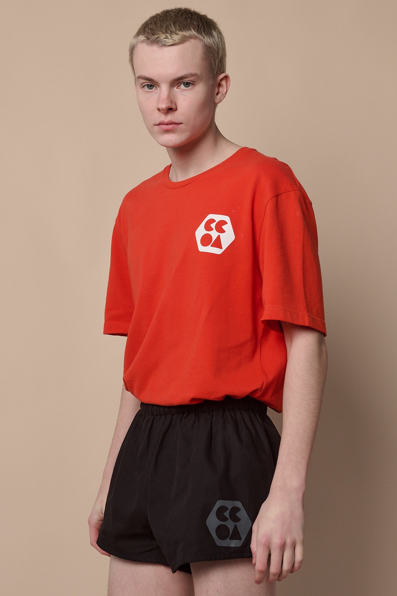 Thigh up image of white male wearing men's lightweight sports short plastic free in black with CCOA logo paired with breathable short sleeve t shirt in flame red.